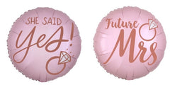 Los Globos Anagrama/MD 18" Blush Wedding son redondos y rosas, con texto en oro rosa. Uno dice "ELLA DIJO SÍ" con un gráfico de anillo de diamantes; el otro dice "Futura señora", también con un gráfico de anillo de diamantes.