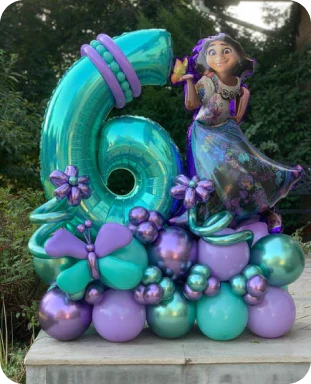 A sixth birthday balloon display in purple and teal featuring butterflies, flowers, a ring, and Mirabel