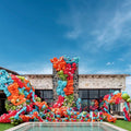 Un bâtiment en pierre est orné de grappes de ballons colorés, notamment des ballons en latex standard rose magenta de 60 cm de Kalisan, qui forment le mot « KALESA » au bord d'une piscine sous un ciel bleu.