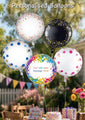 An 18" Oaktree Sparkling Fizz Rose Gold holographic foil balloon floats above a birthday table outdoors, joined by colorful balloons. On the table are a cake, flowers, and a Happy Birthday card.