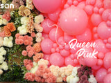 A decorative backdrop featuring 12″ Kalisan Latex Heart Balloons in Queen Pink from Kalisan arranged on the right, accompanied by clusters of colorful artificial flowers on the left.