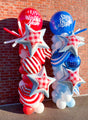 Two balloon columns with Tuftex 18" Circle USA Patriotic Stripes foil balloons stand against a brick wall, accented by silver stars and checkered star designs for festive patriotic décor.
