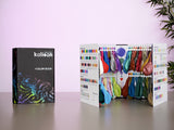 La cartera Kalisan 2026 Latex Balloons Black Color Book está abierta sobre una mesa, mostrando filas de globos de colores y cartas de colores, con la cartera cerrada al lado y una planta al fondo.